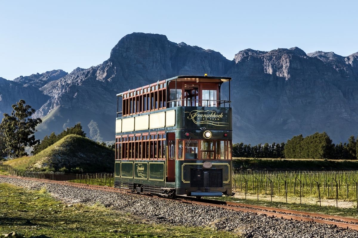 The Franschhoek wine tram on its rails between the vineyards, the mountains standing behind it